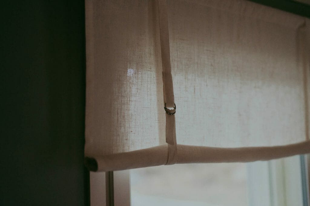 White linen roll up curtain hanging in window.