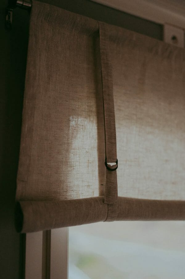 linnefärgad beige rullhissgardin i linne hänger i fönster.