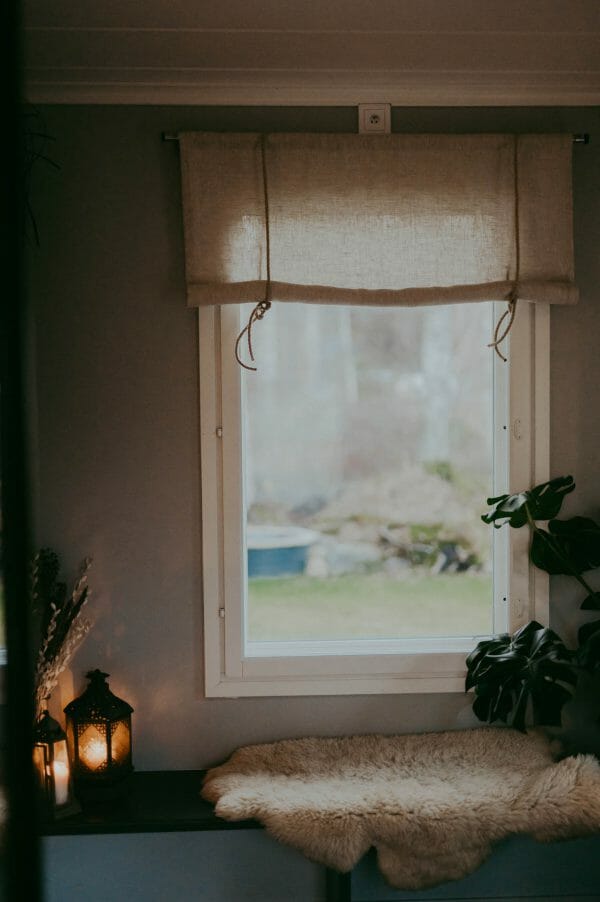 linnefärgad beige rullhissgardin med rep i linne hänger i fönster.